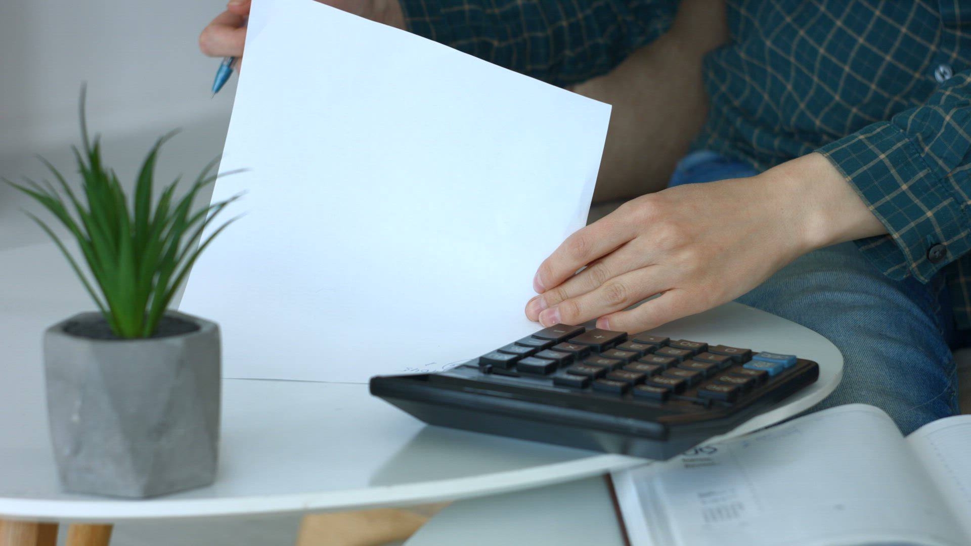 A person reviews a document beside a calculator and an open ledger.