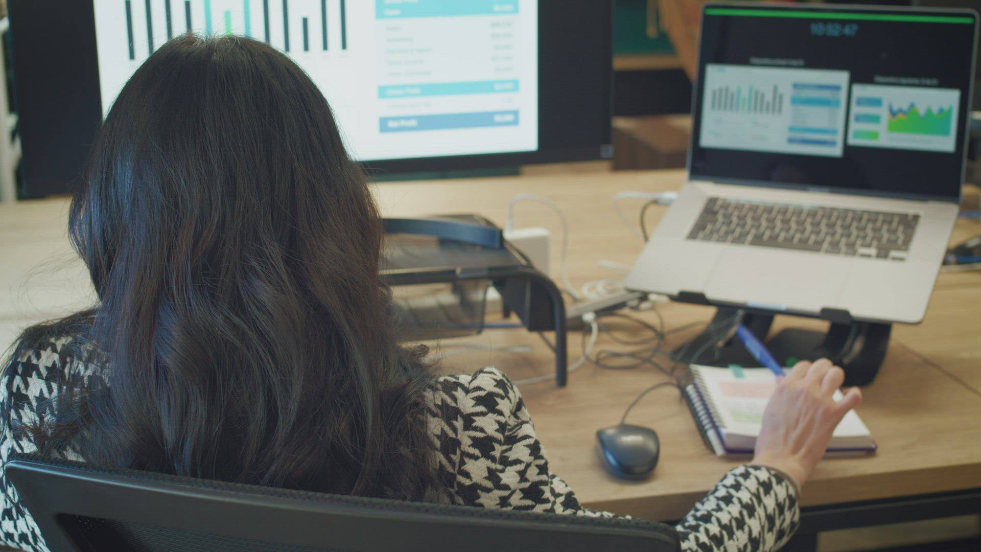A woman reviews charts on two screens at her desk.