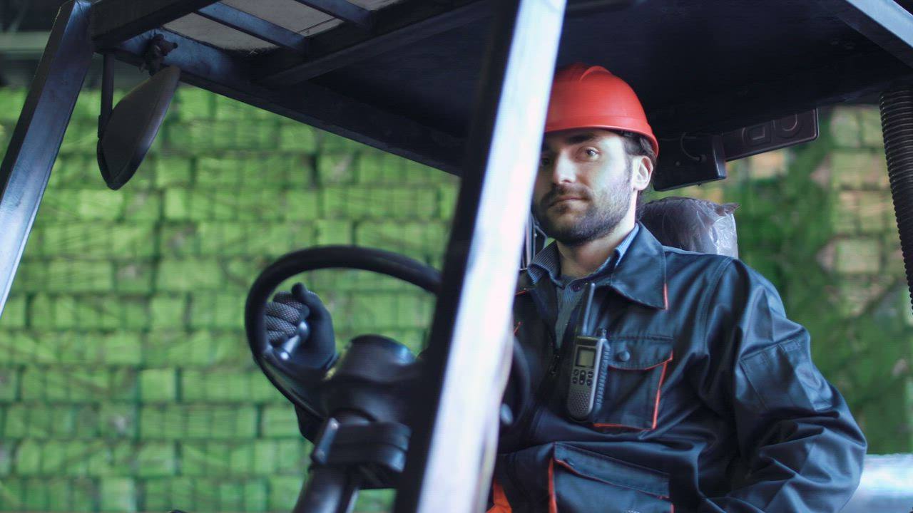 Un operador de montacargas con casco en los controles, dentro de un almacén